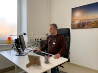 Dr. med. Ralf Kowalzik sitzt an einem Schreibtisch in einem der Behandlungszimmer